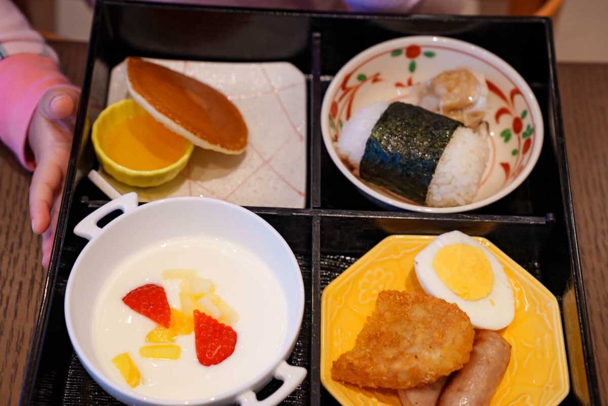 子供用の朝食メニュー。左上からパンケーキ、右におにぎり。左下にヨーグルト、右にゆでたまごとハッシュポテト＆ソーセージ